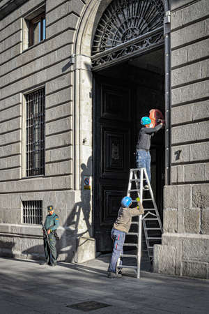 Madrid, Spain - 20 May 2020: Two workers place a camera in an official building using a ladder.のeditorial素材