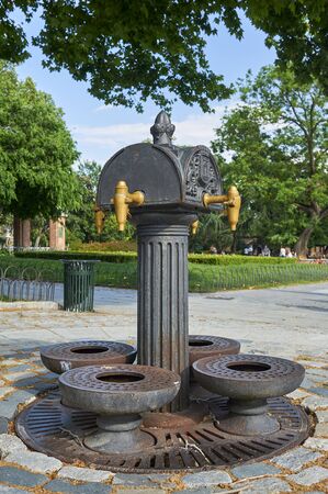 Old public iron fountain in the El Retiro park in Madrid, Spain. Four taps. The background a spring day with clouds in the sky and green vegetation.
の写真素材
