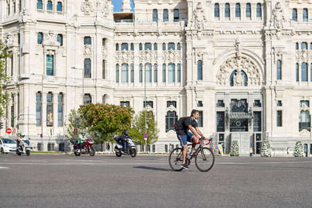 Madrid, Spain - June 15, 2020: Traffic in the Plaza de Cibeles in Madrid. A young man is riding a bicycle and they have a protective mask for the Covid-19.のeditorial素材