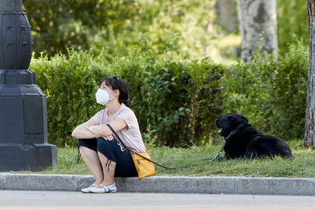 Madrid, Spain - July 7, 2020: A woman with mask rests next to her dog in the parkのeditorial素材