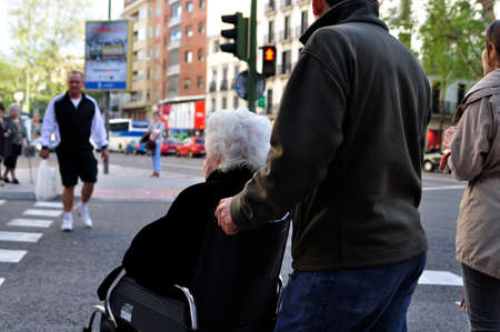 Madrid, Spain - April 20, 2013: Senior lady in a wheelchair crossing a crosswalk with the help of...