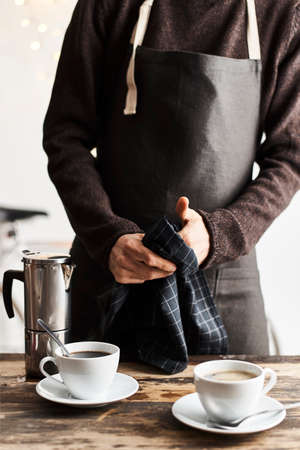 Unrecognizable bartender wiping hands with towel after serving coffee cups.の写真素材