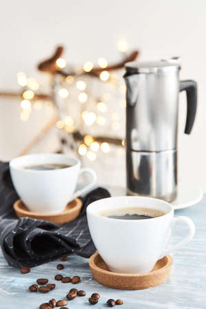 Two cups of fresh tasty coffee and metallic pot on a table.