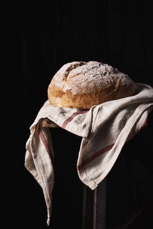 Composed loaf topped with flour on rustic kitchen towel with black background.