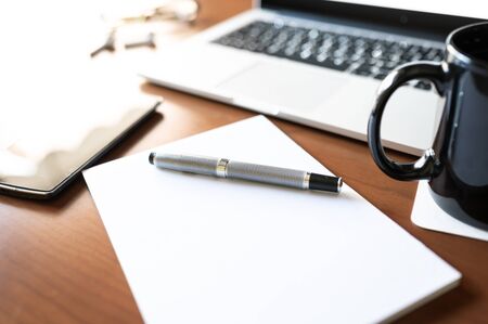 Blank notebook with pen are on the wooden office table with the laptop and a coffee cup. Selective...