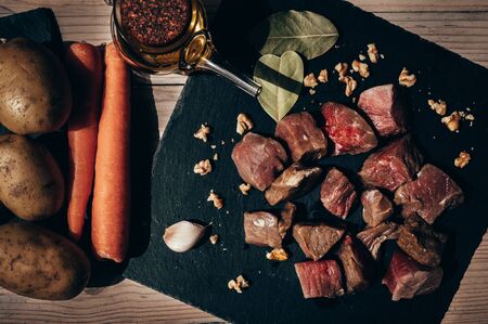 Top view of raw beef cut into a black slate plate with bay leaves and garlic, surrounded by olive oil, carrots and potatoes on a rustic wooden table. Concept of food and life healthy.の写真素材