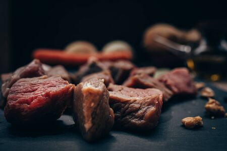Pieces of raw meat on a black board with various ingredients in an unfocused background. Copy space.Concept of dark foodの写真素材