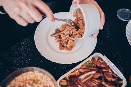 Man's hands hold container with food that he pours into white plate.Enjoying the weekend with the family.の写真素材