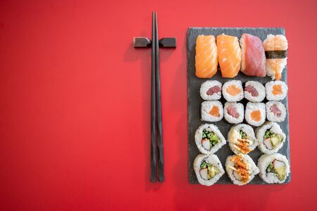 Set of sushi and maki roll.Sushi rolls set with tuna and salmon fish and black chopsticks isolated on red background.Top view.Copy spaceの写真素材