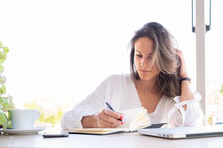 Young entrepreneur writes down in her notebook new ideas for her small business. On the table a cup of coffee, a smart phone and a laptop.Copy spaceの写真素材