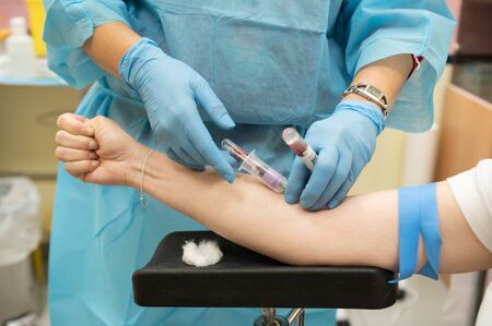Nurse draws a patient's blood while holding a tube of blood previously drawn for Covid 19 test
