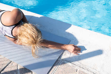Blonde Caucasian girl relaxing by the hotel pool in a sunny day.Vacation and tourism concept