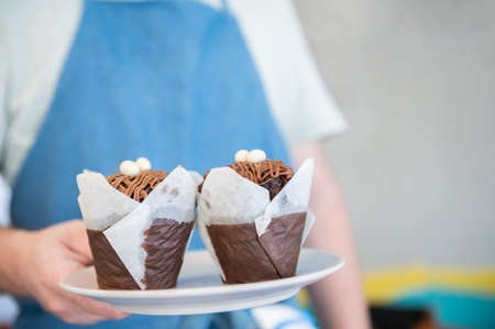 A coffee shop waiter holding a plate with two appetizing muffins.Copy space.Sweet moments. Small...