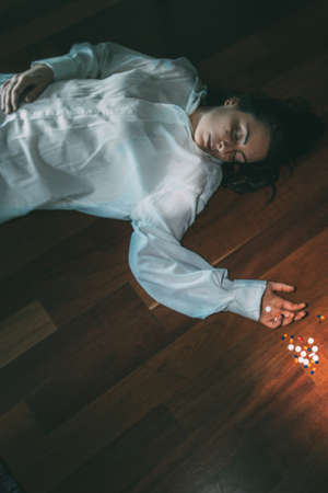 Young nice girl lie on the wooden floor after overdose of medical pills.Top view.Copy space.Suicide...