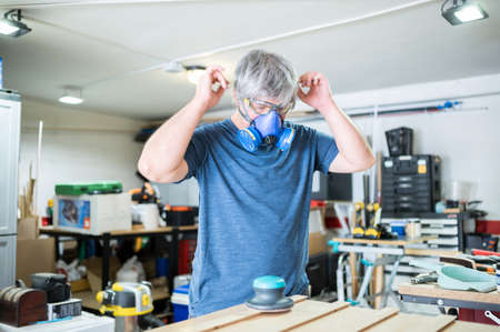 Carpenter man wears a mask to protect himself from dust in his workshop