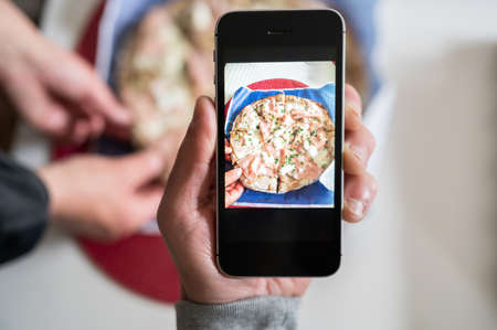 Young man an taking photo with smart phone of a pizza during a friends meal.Copy spaceの写真素材