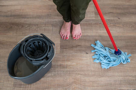 Close up of young barefoot woman with red painted nails scrubbing a wooden floor.の写真素材