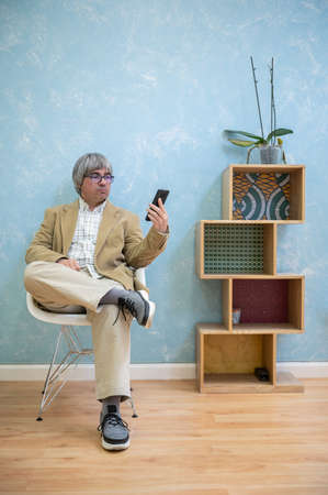 Man with glasses looking at his mobile phone in a nice and colorful dental clinic waiting room....