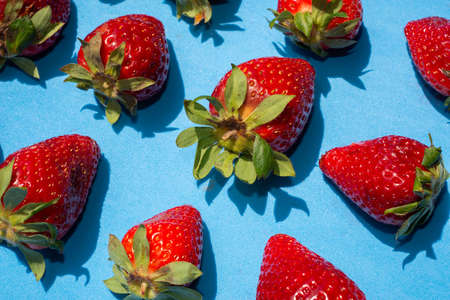 Top view of several red strawberries with green leaves on a blue background.Healthy food concept.