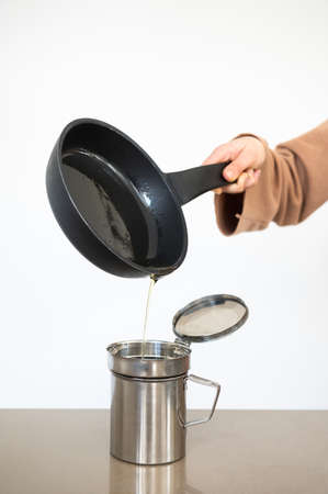 Woman pouring used cooking oil from an old frying pan into a metal cooking container.Oil recycling...