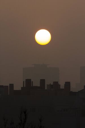 Sunset with a big round sun on a city with fog. Brown and orange coloursの写真素材