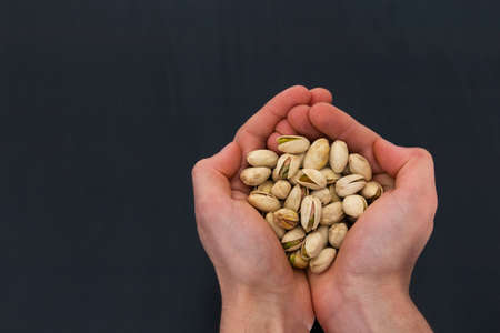 a person holding pistachios on his hands with black background and copy spaceの写真素材