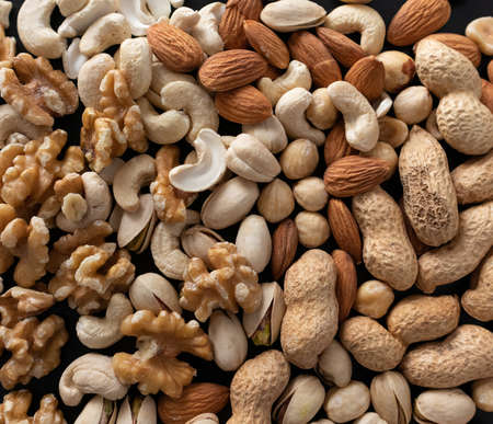 a mixture of nuts (peanuts, pistachios, almonds, walnuts, hazelnut, cashew) from top view with black...