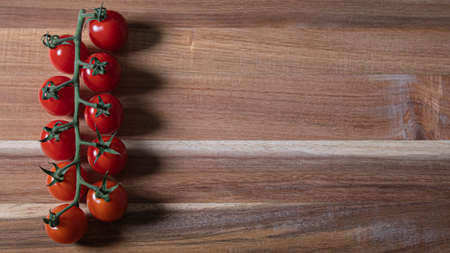 Small deep red cherry tomatoes on a branch on a weathered wooden boardの写真素材