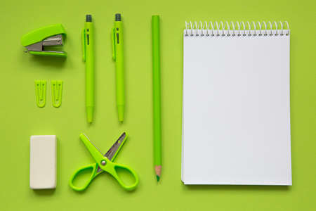 Green school supplies next to a small notebook with a blank page