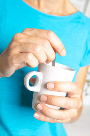 Woman in blue t-shirt holding and drinking from a cup of tea in her break timeの写真素材