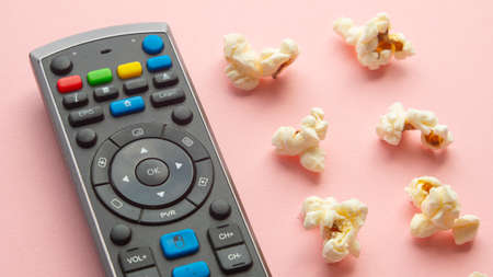 Popcorn on a light pink background next to a television remote controlの写真素材