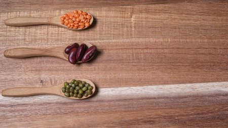 Legumes of different types such as red lentil, green soybean and bean on wooden background