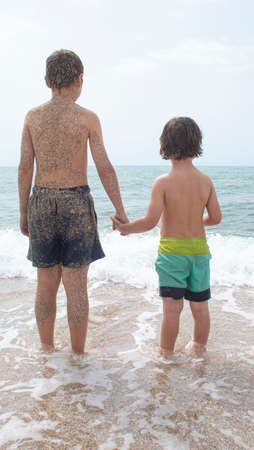 Children with their hands clasped in a swimsuit and with their backs looking at the beachの写真素材