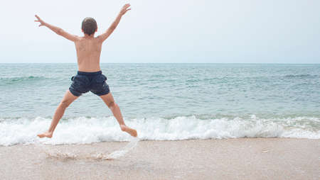 Boy from behind jumping for joy and from behind looking at the beach