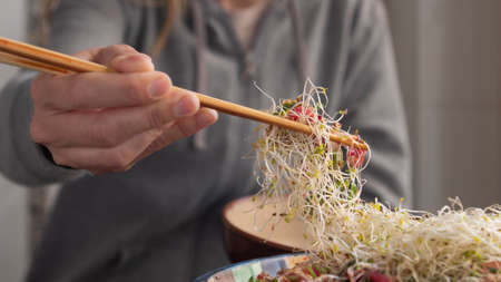 Hand with chopsticks picking up sprout salad from a bowlの写真素材