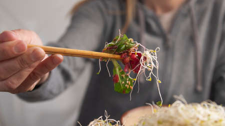Hand with chopsticks picking up sprout salad from a bowlの写真素材