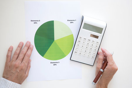 Hands of a middle-aged woman checking and analyzing a graph using a calculator. Paper with green statistical pie chartの写真素材
