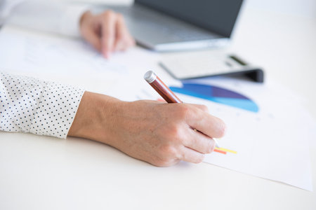 Hands of middle aged woman in white shirt working on financial statistics with her laptop and calculatorの写真素材