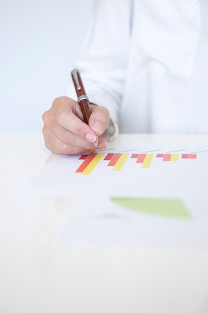Detail of hands of middle-aged woman in white shirt working with documents with financial graphs and statisticsの写真素材