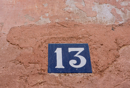 Blue ceramic square brick on old wall with the number thirteen painted in white color.の写真素材
