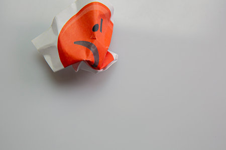 Square piece of paper with the face of an angry emoji