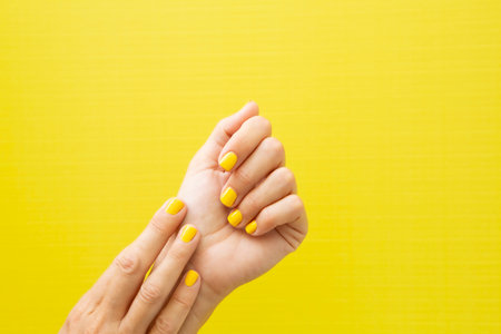 Horizontal photograph of a woman's two hands with her nails painted yellow.の写真素材