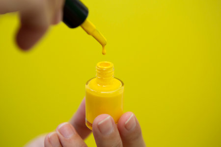 Horizontal photograph of a woman's hand painting her nails yellow in front of a yellow background.の写真素材