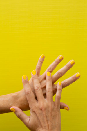 Vertical photograph of a woman's hands with her nails painted yellow on a yellow background.の写真素材