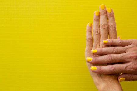 Horizontal photograph of a woman's hands with her nails painted yellow on a yellow background.の写真素材