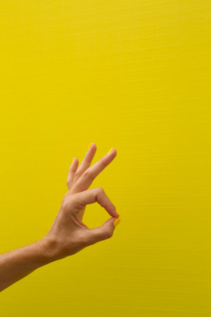 Vertical photograph of a woman's hand with her nails painted yellow, giving a thumbs-up gesture.の写真素材