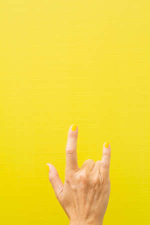 Vertical photograph of a woman's hand making the typical heavy metal horns with her nails painted yellow.の写真素材