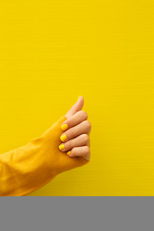 Vertical photograph of the hand with yellow fingernails holding the sleeve of the yellow shirt.の写真素材