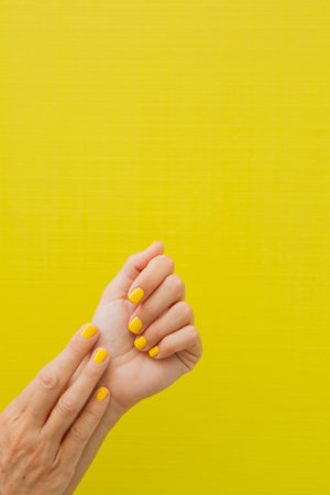 Vertical photograph of a woman's two hands with her nails painted yellow.の写真素材