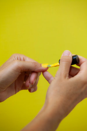 Vertical photograph of a woman painting her nails yellow on a yellow background.の写真素材